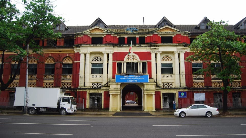 A large, ornate building with a red and yellow facade, a central archway, and a flagpole.