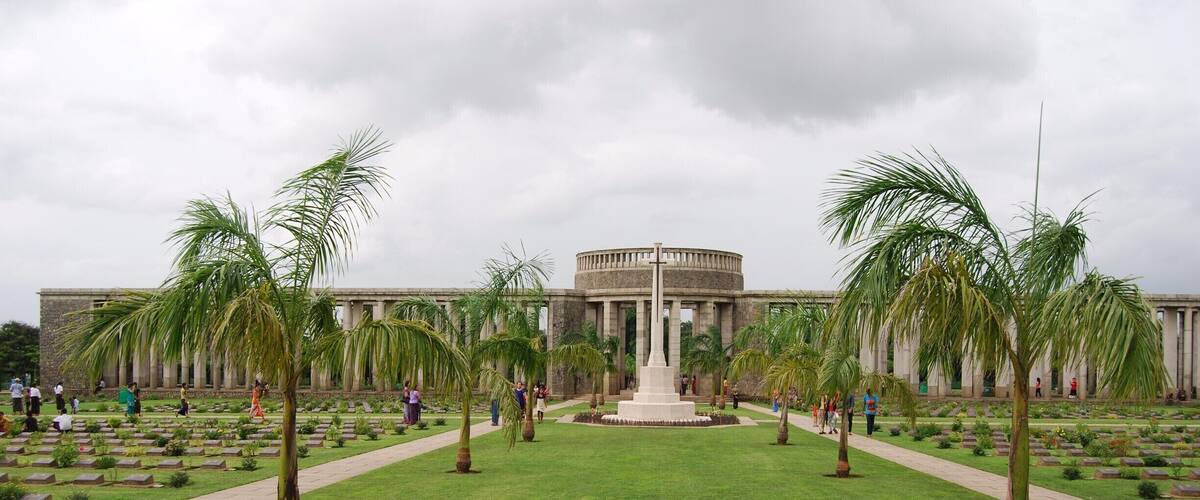 A large, circular building with a central monument surrounded by palm trees and a well-maintained lawn.
