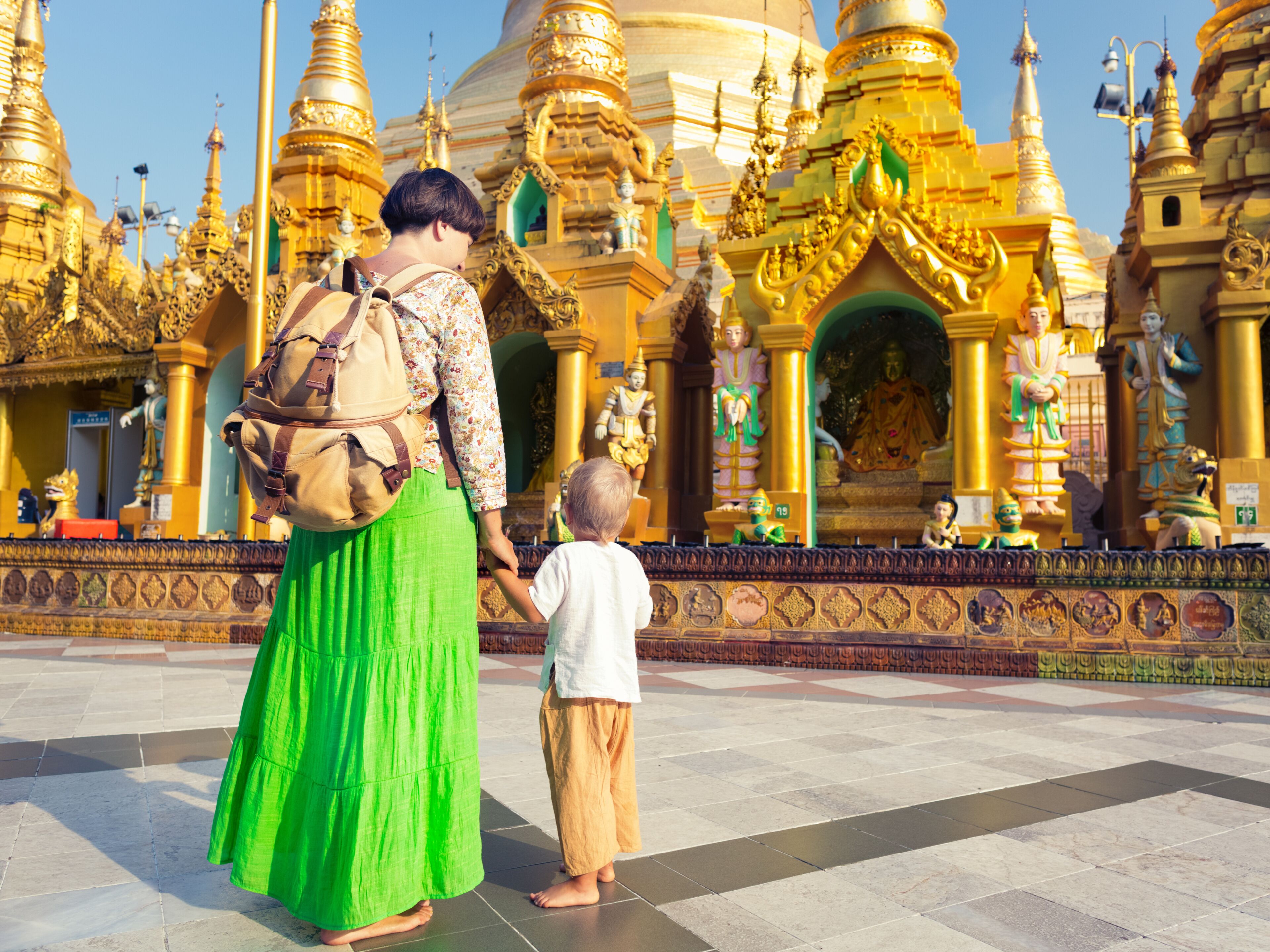 Una mujer y un niño caminando frente a un templo dorado de arquitectura intrincada.