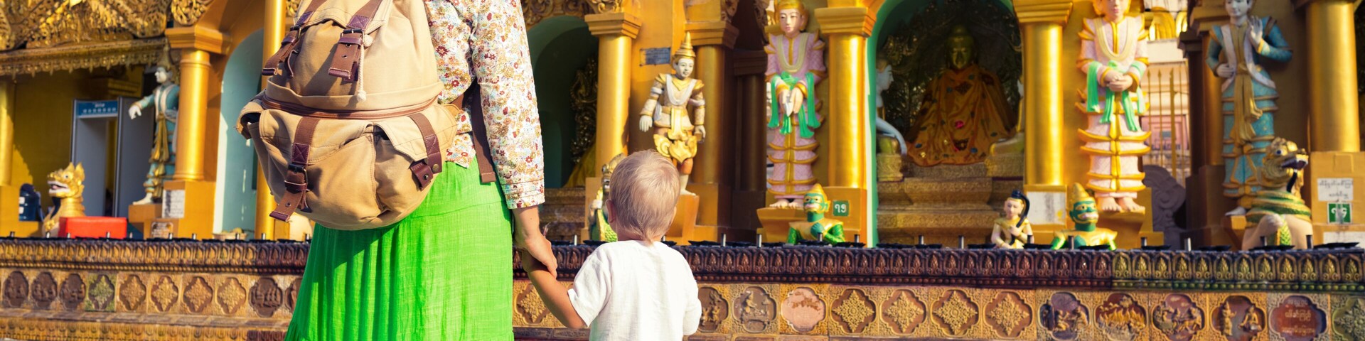 Una mujer y un niño caminando frente a un templo dorado de arquitectura intrincada.