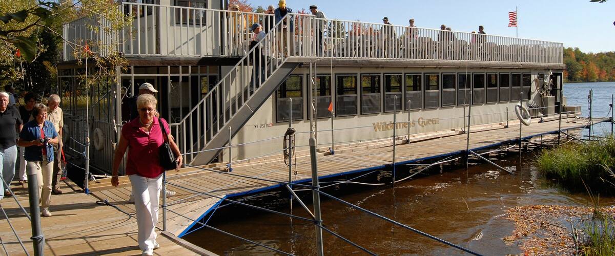 A riverboat docked at a pier with people boarding and disembarking.