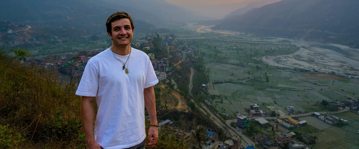 A person standing on a hill overlooking a valley with a river and buildings.