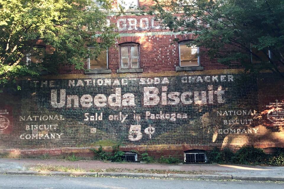 Un bâtiment en briques sur lequel est apposée une grande enseigne publicitaire pour les biscuits « Uneeda » et la « National Biscuit Company ».