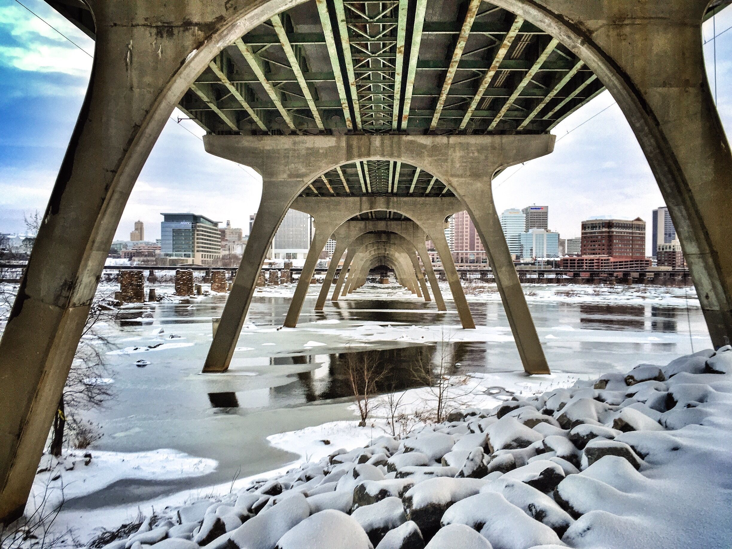 On a recent snow day, I took a walk along the Flood Wall, and found myself under the Manchester Bridge that spans the James River in Richmond. This bridge was built to replace the old Ninth Street Bridge, which was susceptible to flood damage (you can see the ruins of this bridge in the left side of the photo if you look close enough). #architecture