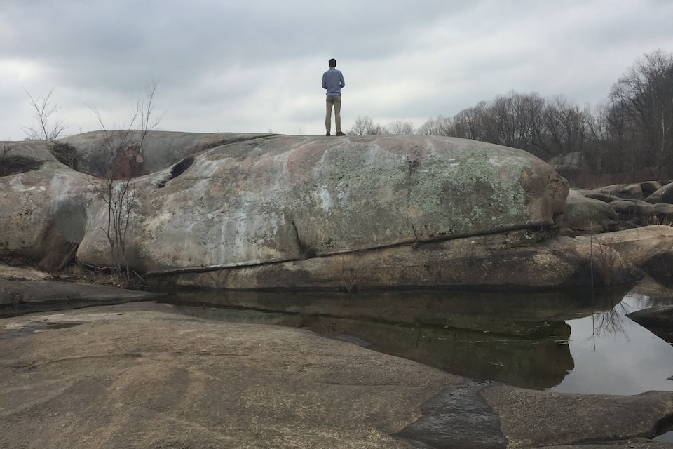 A person standing on a large rock formation with a body of water in the foreground.