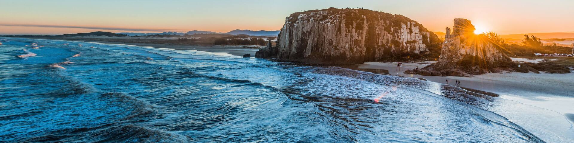 A coastal landscape with a large rock formation and waves crashing onto the shore.