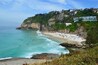 Une plage côtière où l’on peut se baigner et bronzer, entourée d’une végétation luxuriante et de bâtiments situés sur une colline.