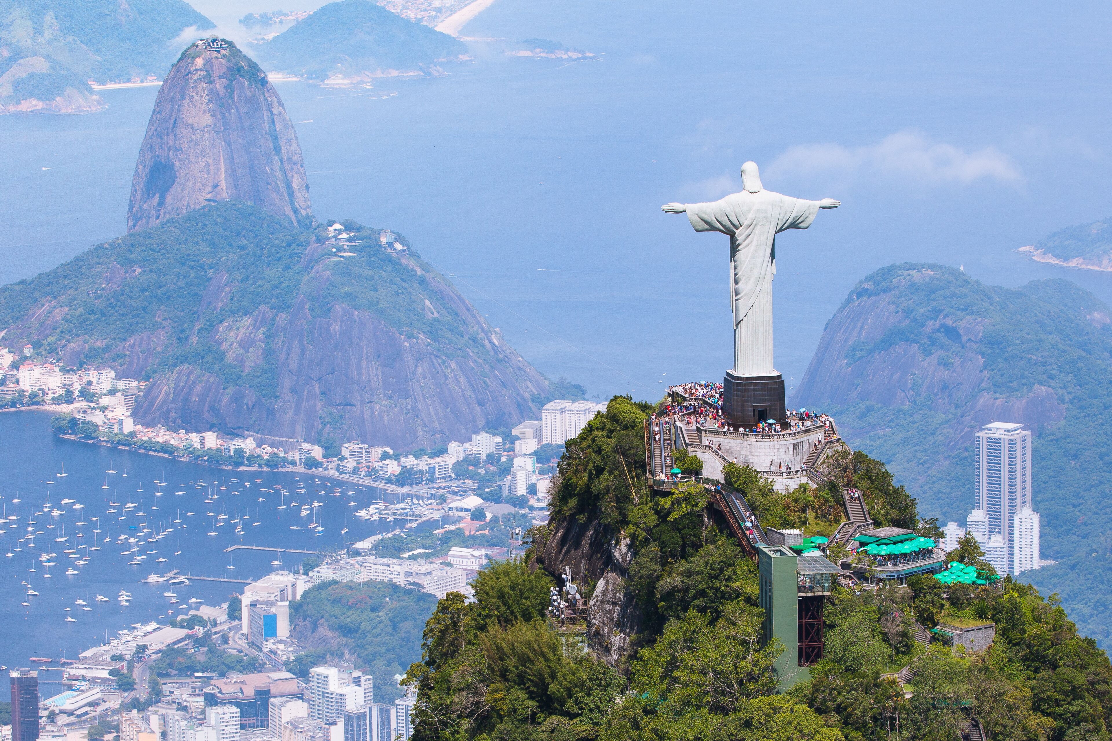 Uma estátua numa colina, com vista para a paisagem urbana e montanhas ao fundo.