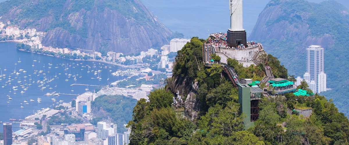 Uma estátua numa colina, com vista para a paisagem urbana e montanhas ao fundo.