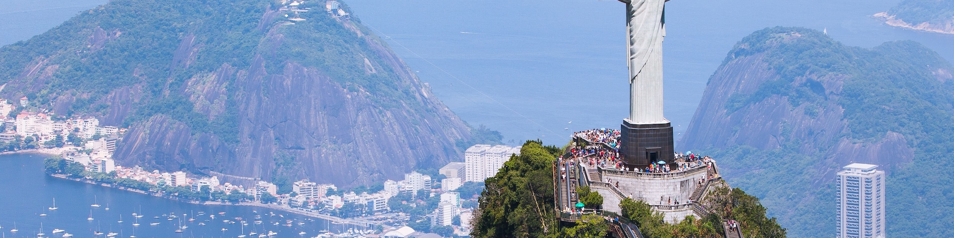 Uma estátua numa colina, com vista para a paisagem urbana e montanhas ao fundo.