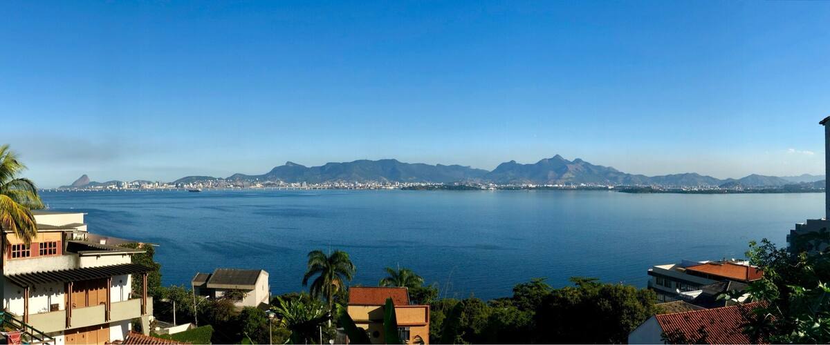 A coastal cityscape with a clear view of the ocean, mountains in the distance, and residential buildings.