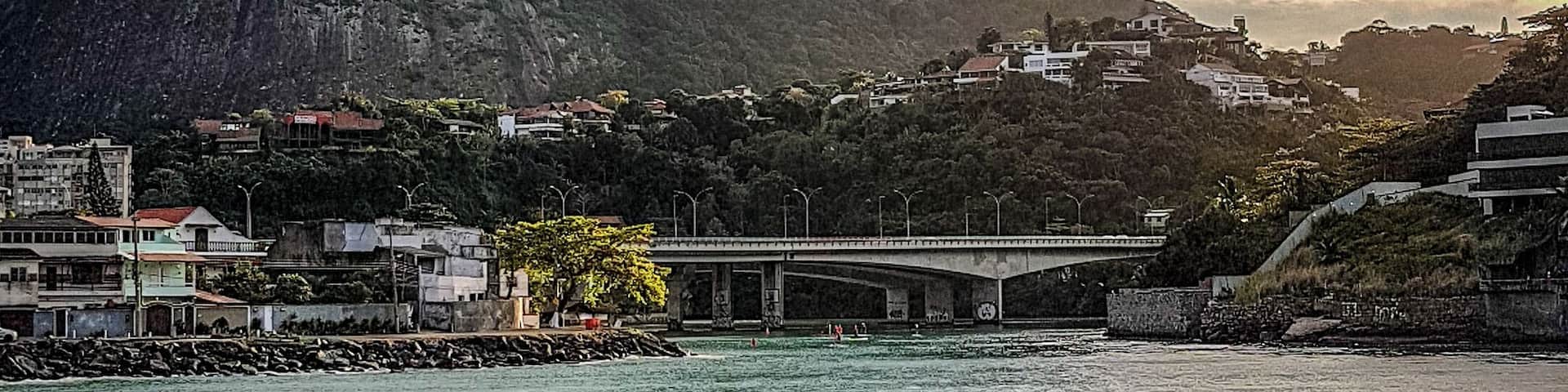 A coastal landscape with a prominent mountain, a bridge, and a rocky shoreline.