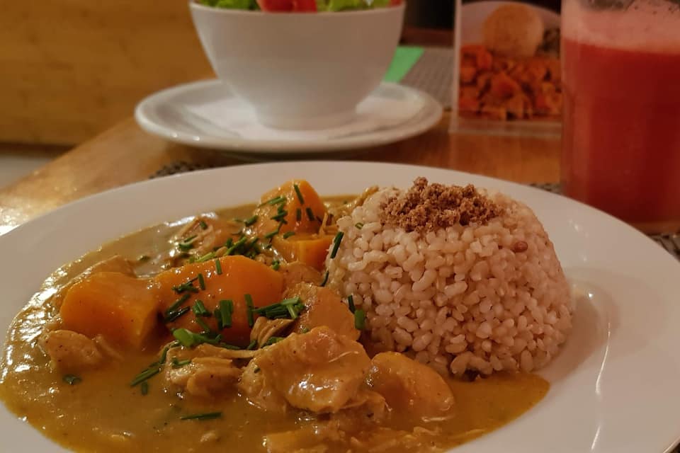 A plate of curry with rice and a glass of red drink on a table.