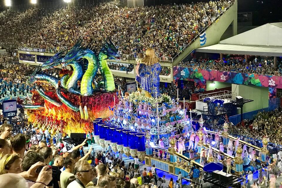 A crowded outdoor event with a large dragon float and performers.