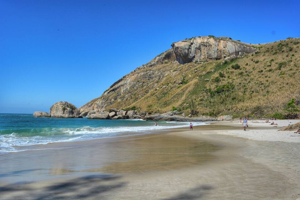 A beach with a rocky hill and ocean waves.