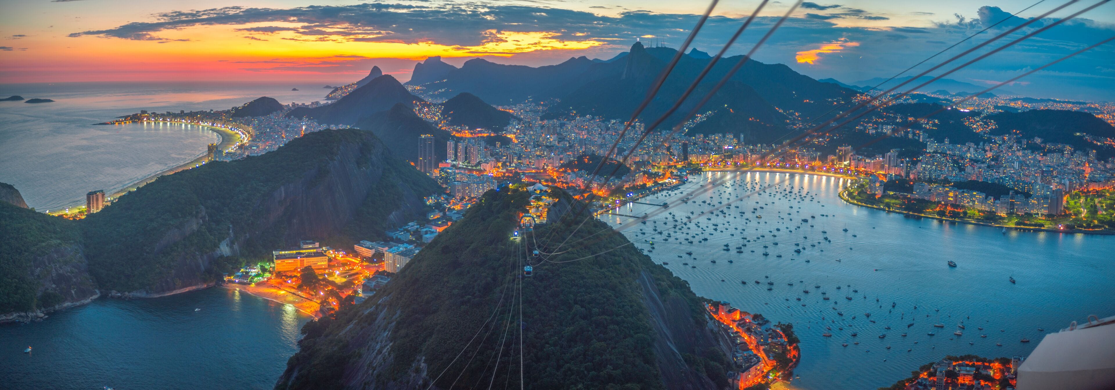 Vista panorâmica de uma cidade costeira com um sistema de teleférico, montanhas e uma baía cheia de barcos.