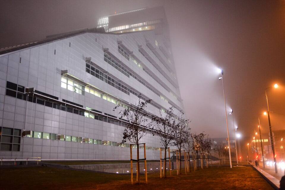Un bâtiment moderne doté d’une façade réfléchissante et bordé d’une rangée d’arbres.