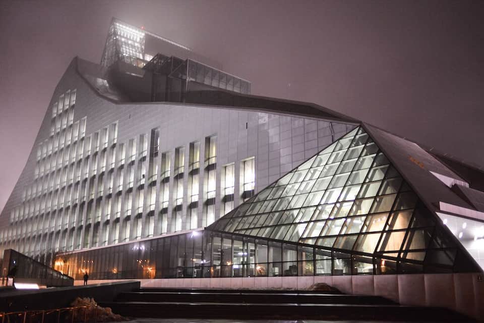 A modern glass building with a unique triangular glass facade and a large, illuminated top section.