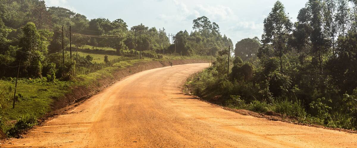 A winding dirt road through a rural landscape with greenery and trees.