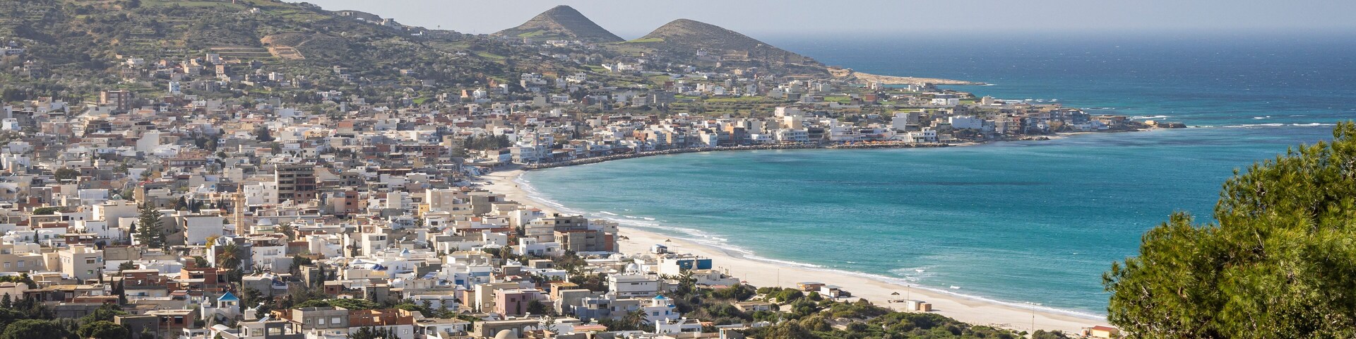 Uma vila costeira com praia, edifícios e colinas.
