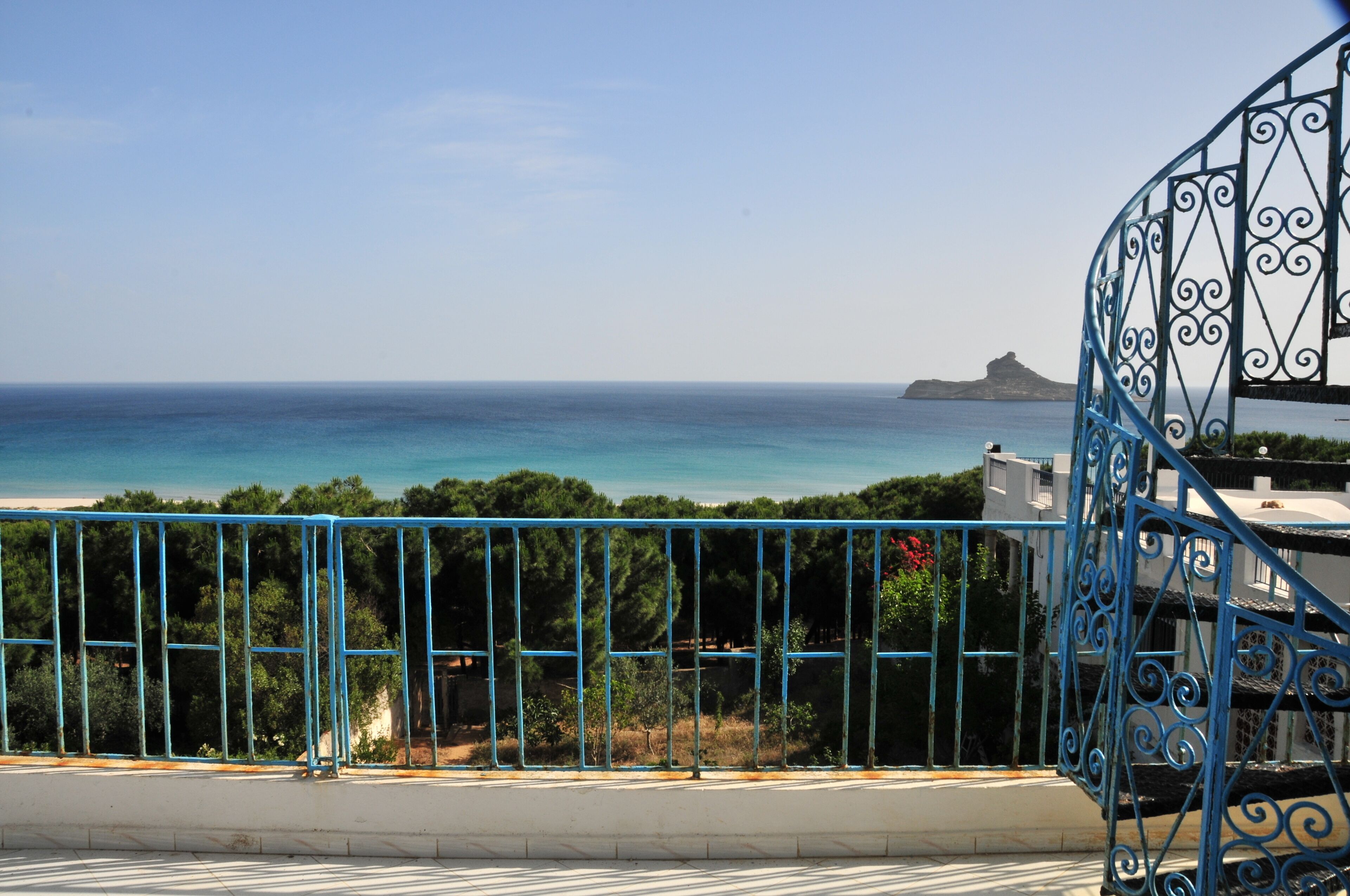 A coastal view with a metal railing, trees, and a distant island.