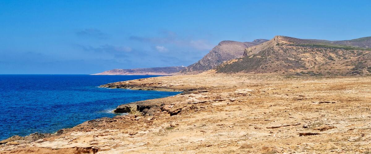 A coastal landscape with rocky terrain and a clear blue sea.