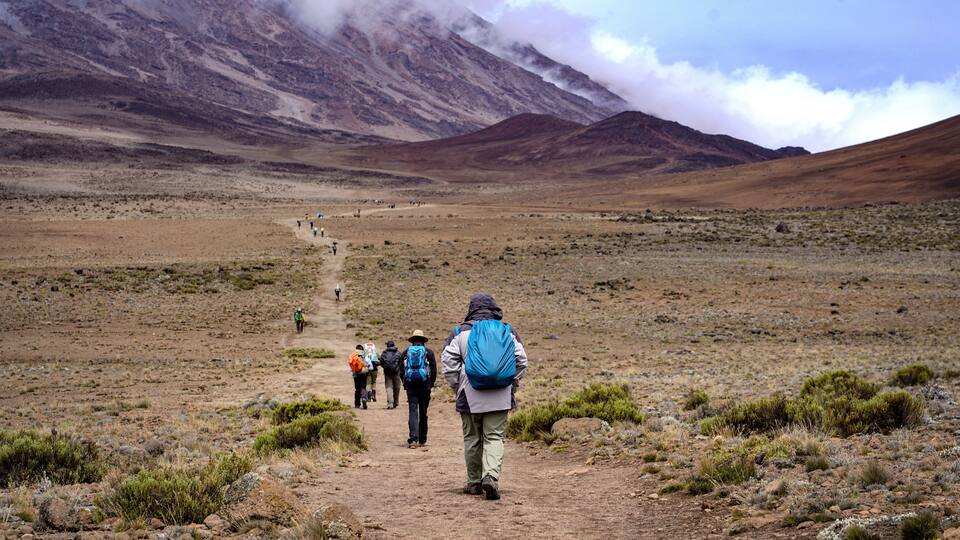 A group of hikers on a dirt trail in a barren landscape with mountains in the background.
