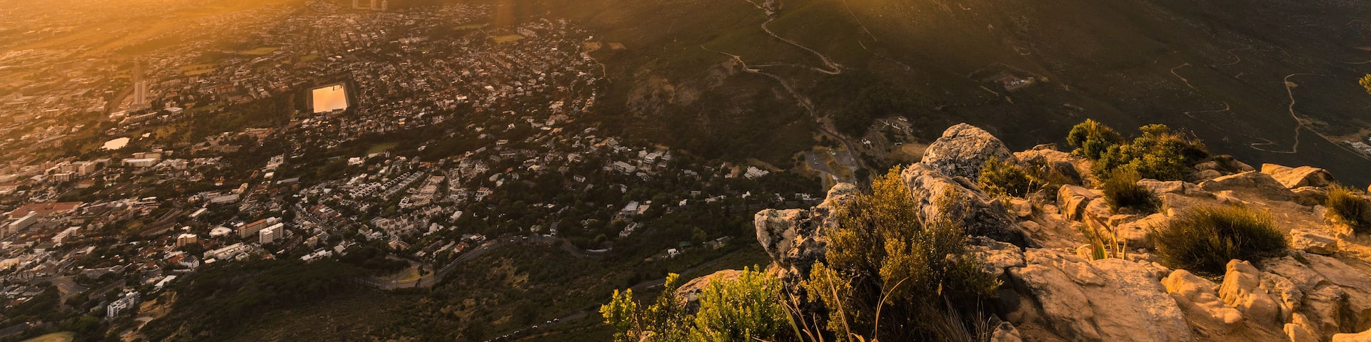 A mountain with a city in the valley below, a river, and a sunset.