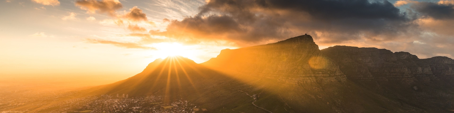 Una montaña con una ciudad en el valle, un río y un atardecer.