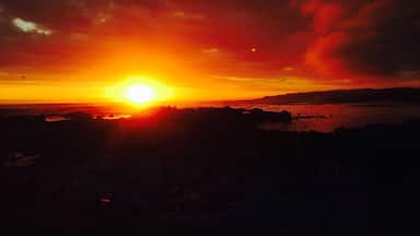 A sunset over a coastal landscape with silhouettes of land and water.