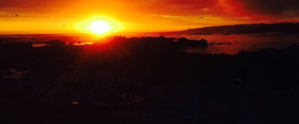 A sunset over a coastal landscape with silhouettes of land and water.