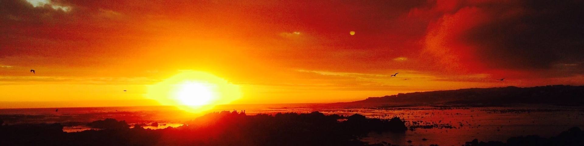 A sunset over a coastal landscape with silhouettes of land and water.