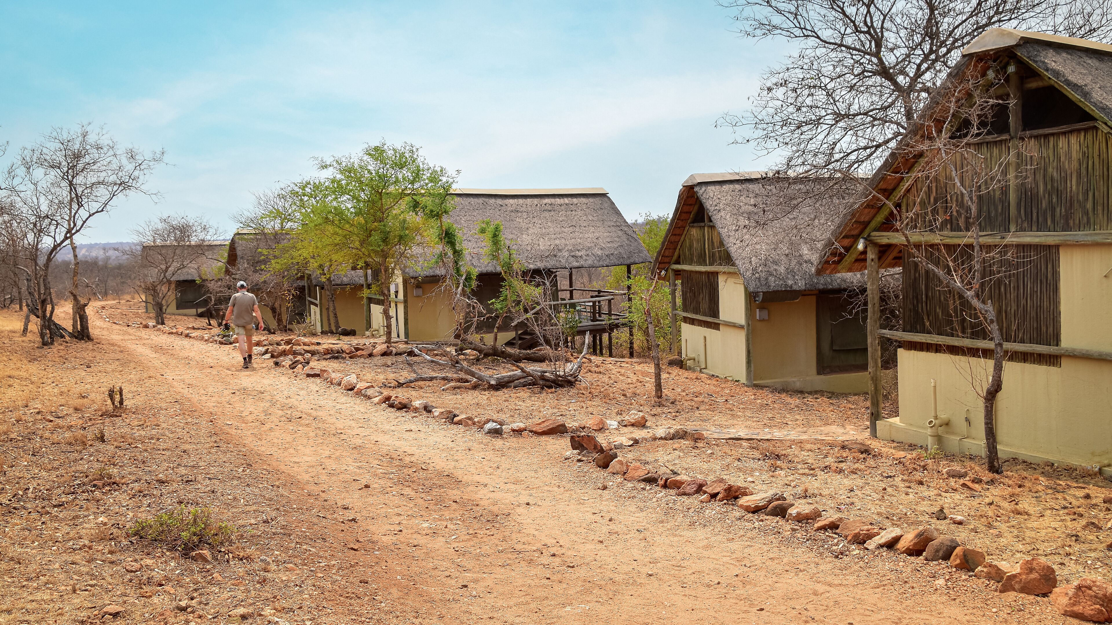 A rural area with thatched-roof huts, a dirt path, and sparse vegetation.