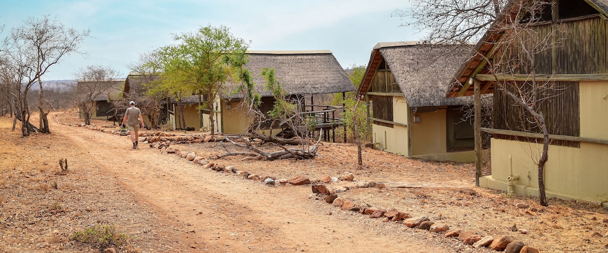 A rural area with thatched-roof huts, a dirt path, and sparse vegetation.