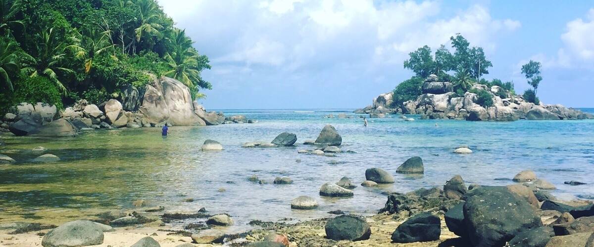A tropical beach with clear water, rocks, and lush greenery.