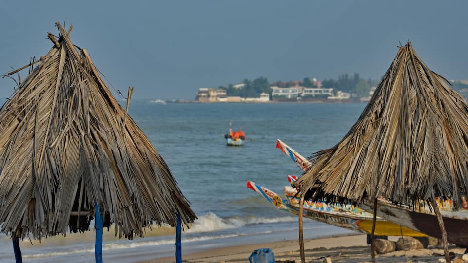 A beach with thatched umbrellas and a boat with colorful decorations.