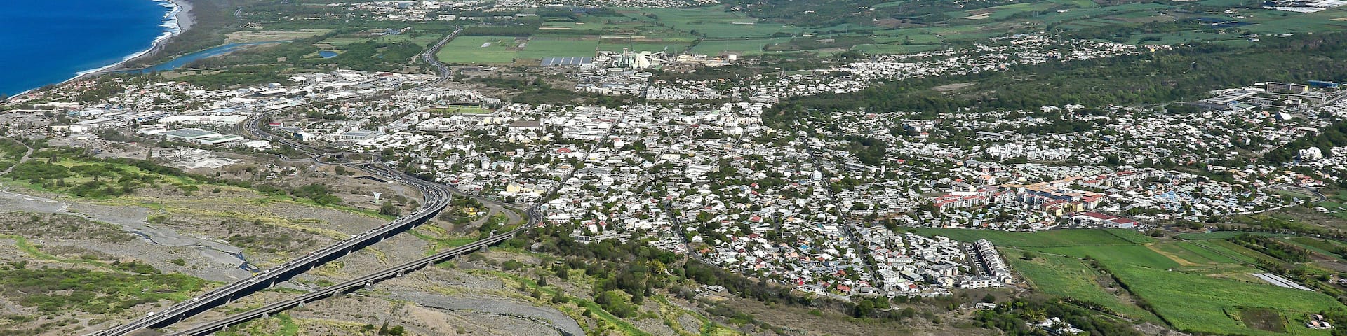 A coastal town with a bridge connecting to the mainland, surrounded by green hills and a clear blue sky.
