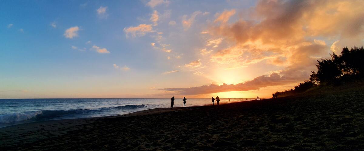 A beach with people walking, a sunset, and a clear sky.