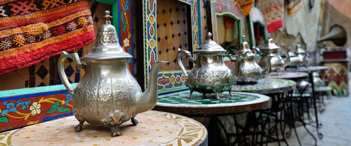 Ornate metal teapots on a patterned table, colorful textiles, and traditional architecture.