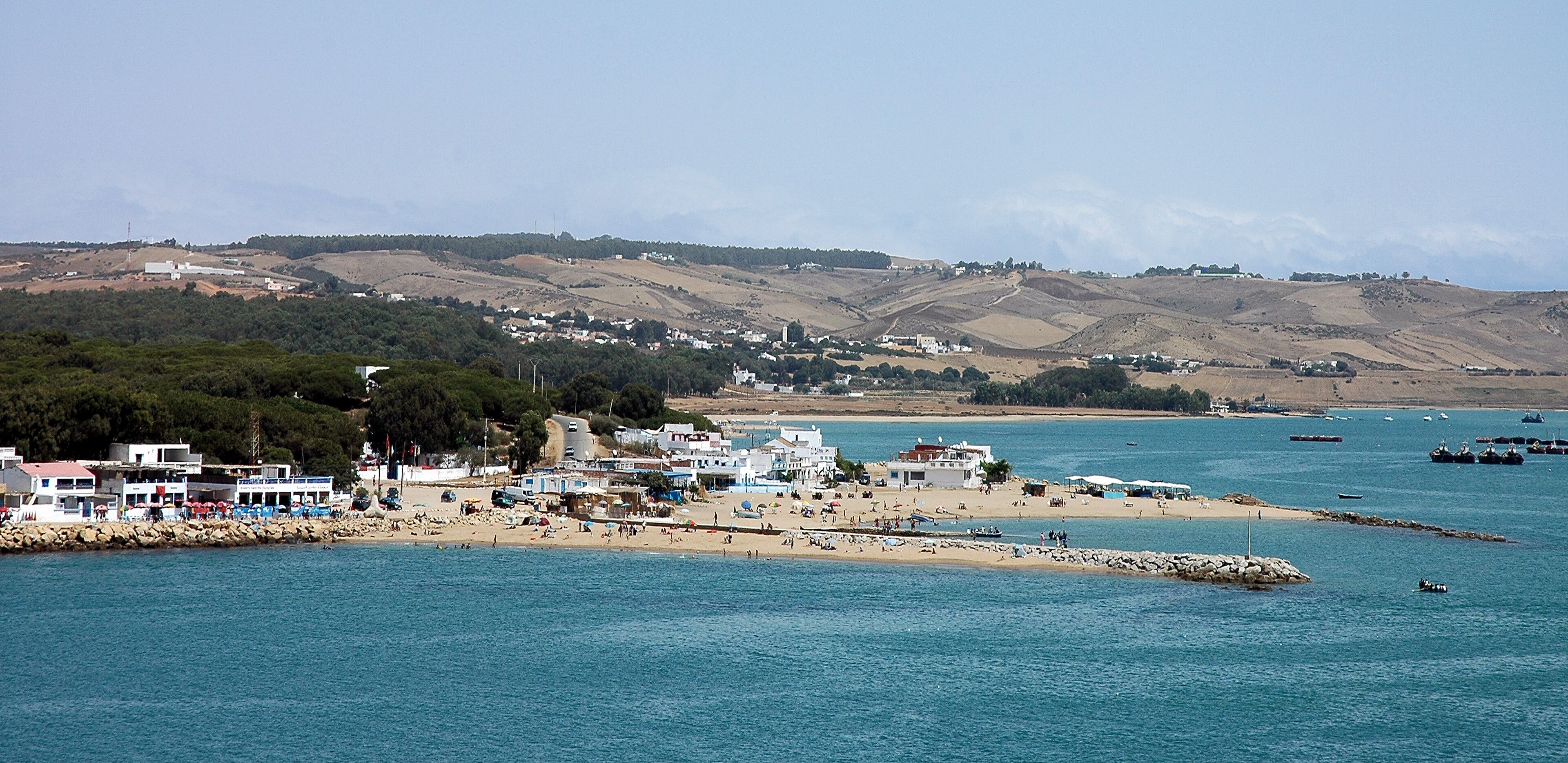 A coastal town with a sandy beach, rocky shoreline, and hills in the background.