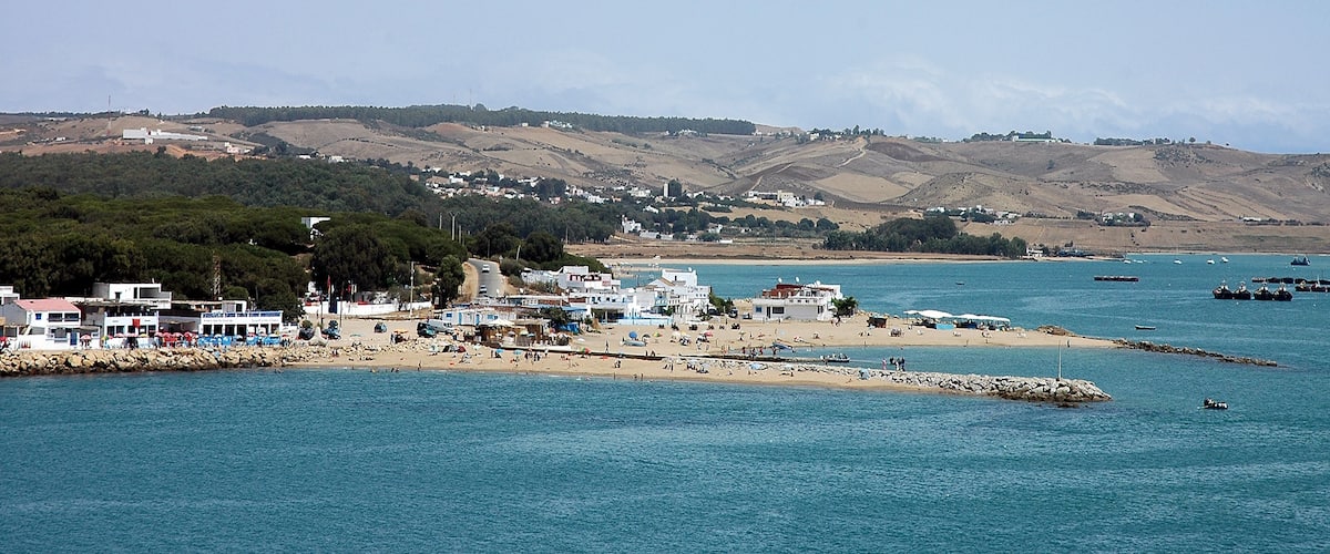A coastal town with a sandy beach, rocky shoreline, and hills in the background.
