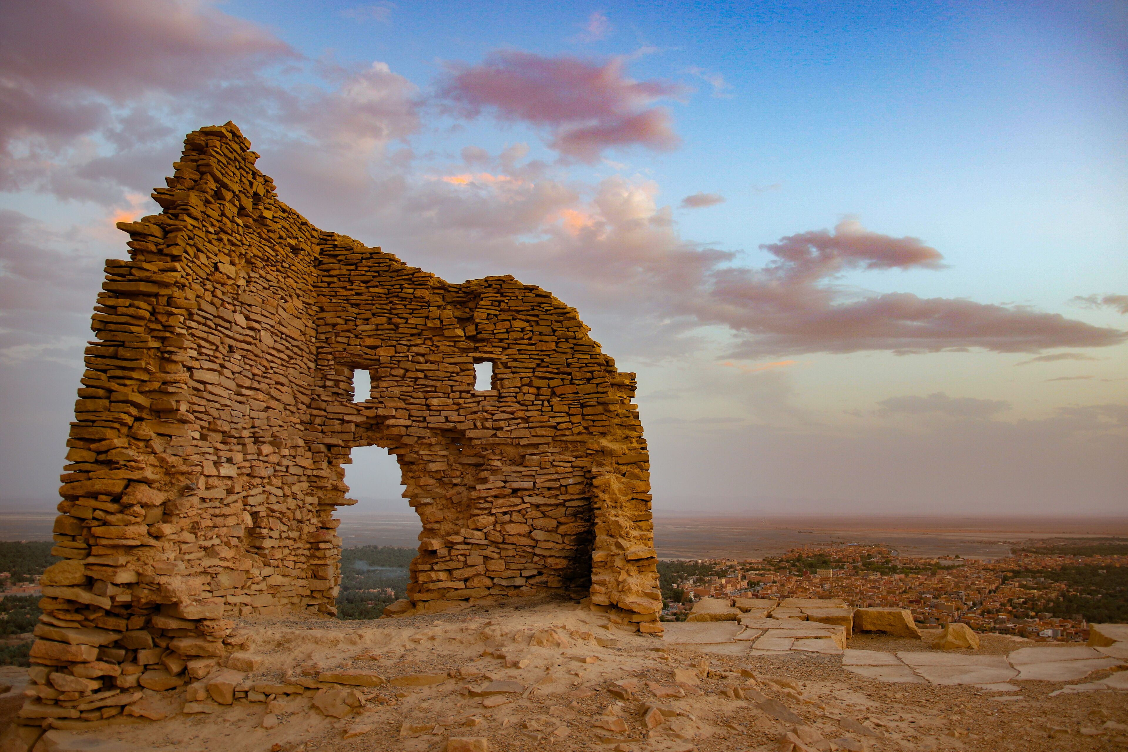 A stone ruin with an arched doorway, surrounded by a desert landscape and a distant city view.