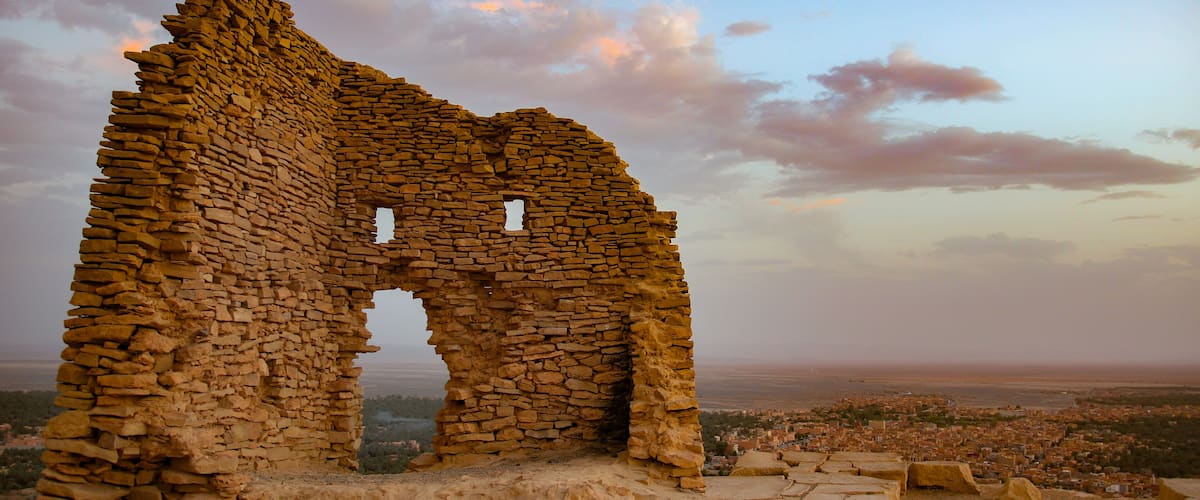 A stone ruin with an arched doorway, surrounded by a desert landscape and a distant city view.
