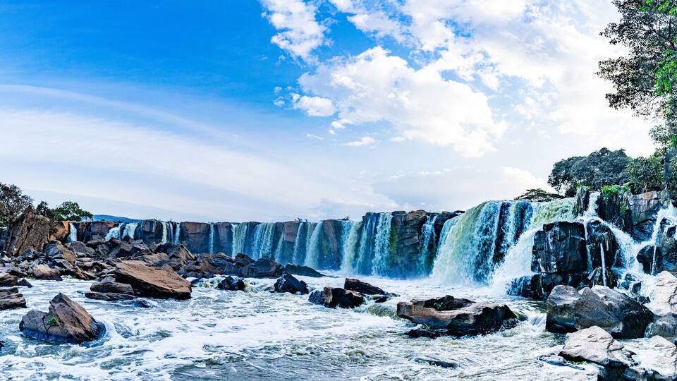 A multi-tiered waterfall with rocky terrain and trees.