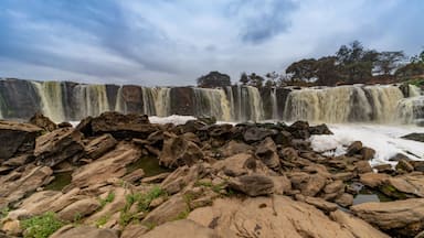 Uma cascata descendo sobre terreno rochoso sob um céu nublado.