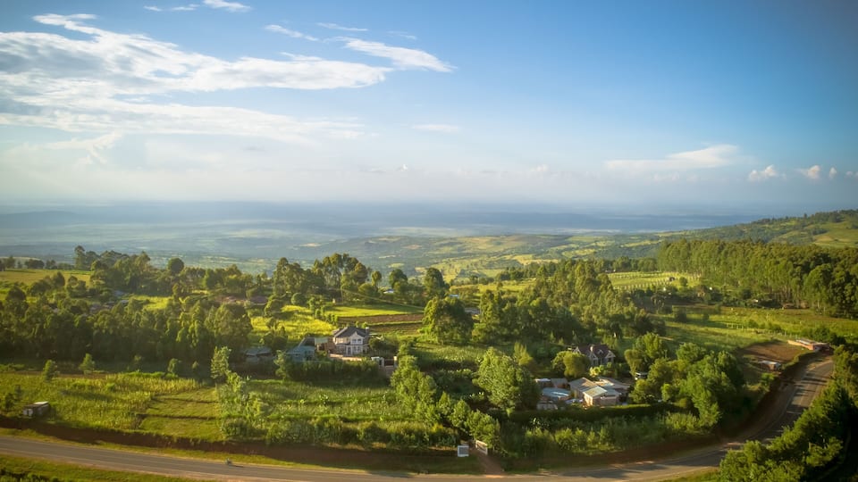 A rural landscape with rolling hills, scattered houses, and a winding road.