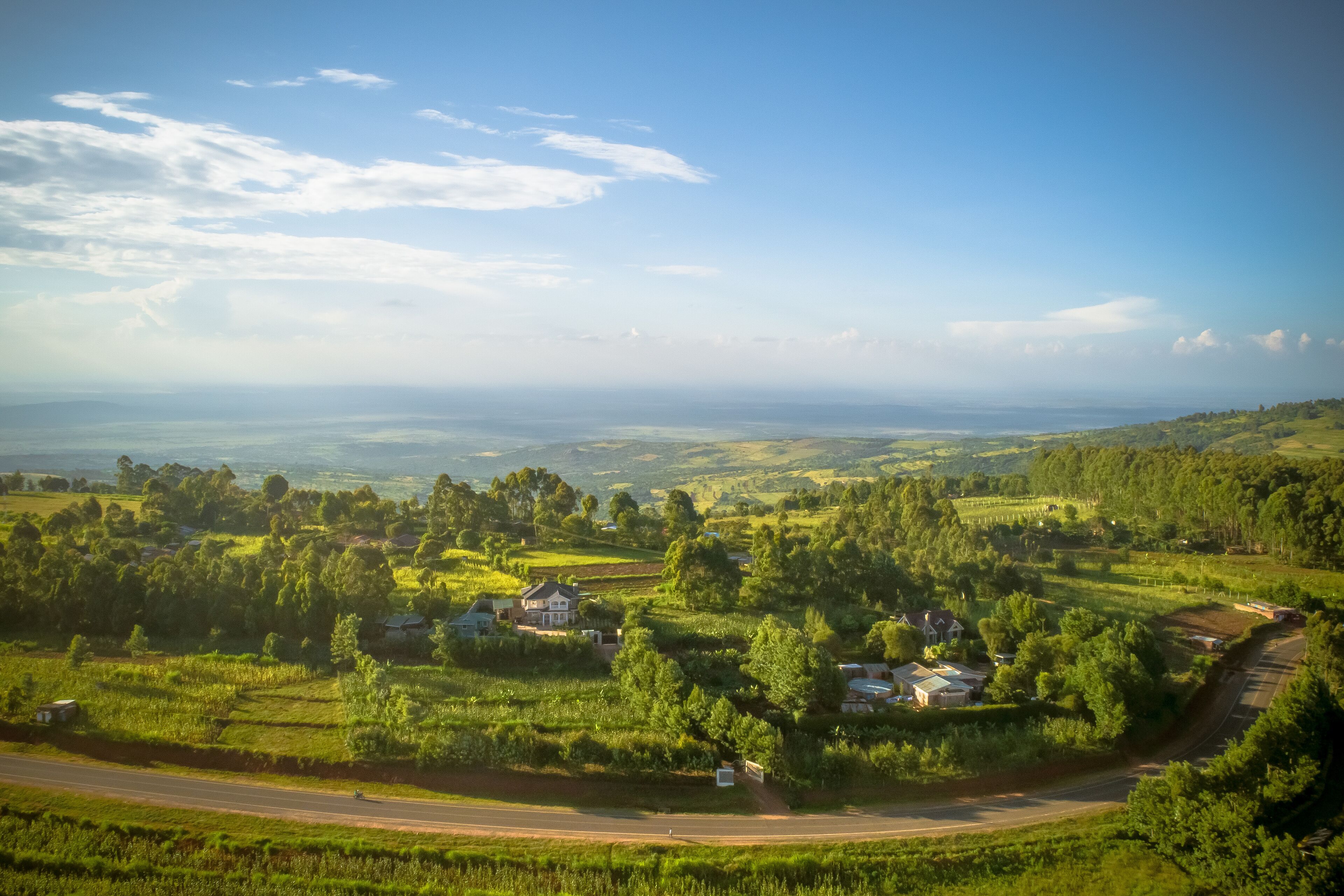 A rural landscape with rolling hills, scattered houses, and a winding road.