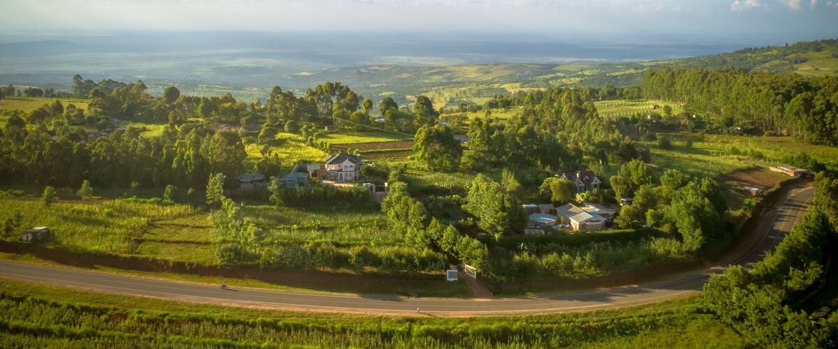 A rural landscape with rolling hills, scattered houses, and a winding road.