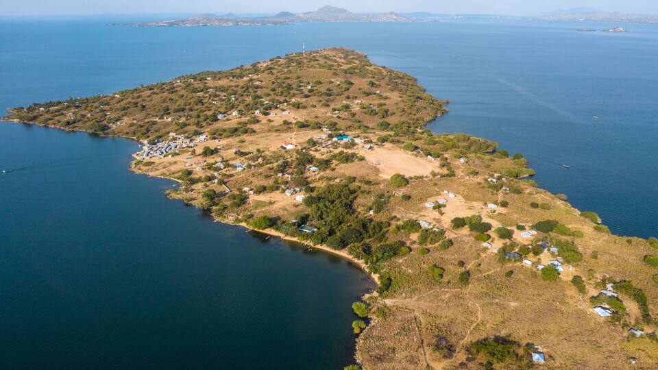 An aerial view of a coastal island with scattered houses and a lighthouse in the distance.