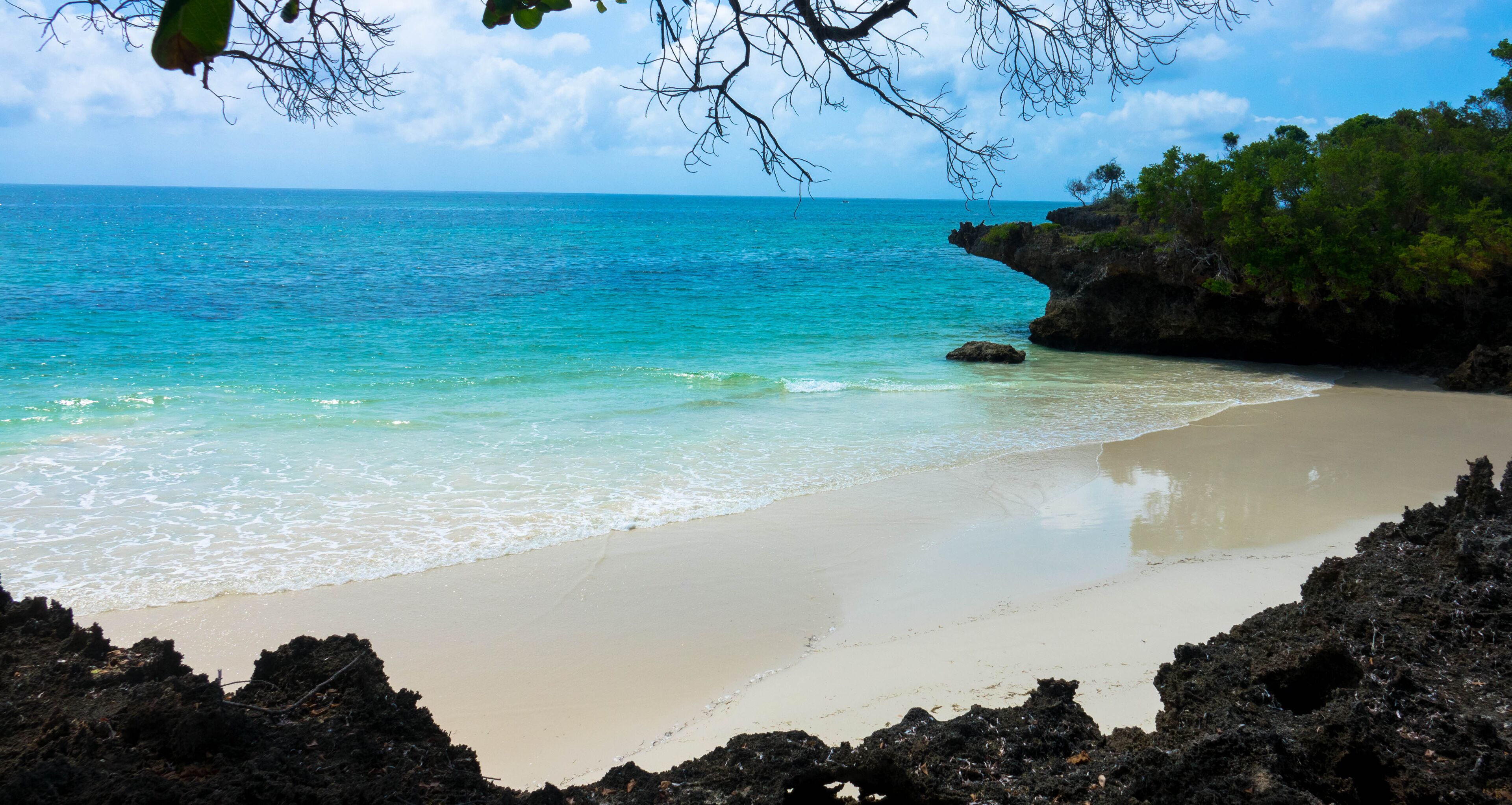 A beach with clear turquoise water, a sandy shore, and rocky outcrops.